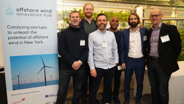 A group of men standing next to a poster promoting "Offshore Wind Innovation Hub"