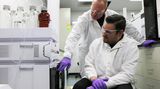 Grad student in lab coat with professor  in the lab