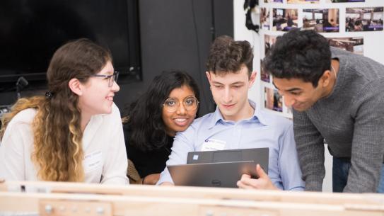 male and female students huddled around laptop smiling