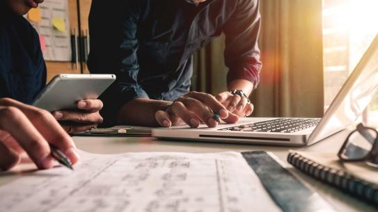 Two people looking at digital devices with work papers