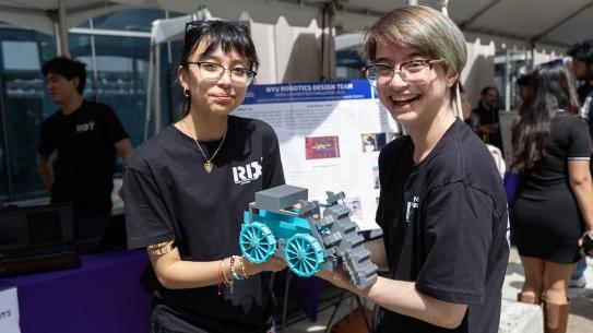 two members of the NYU Robotics Design Team hold up a small robotic vehicle
