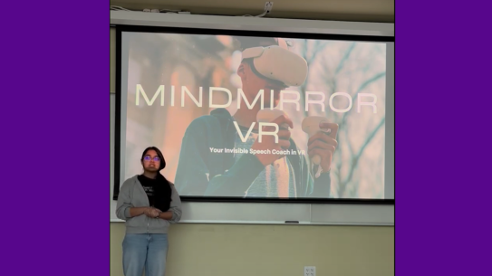 A student delivering a presentation in front of a screen displaying someone wearing VR headgear