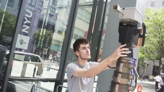 A student adjusting large pice of equipment in front of building on Tandon campus