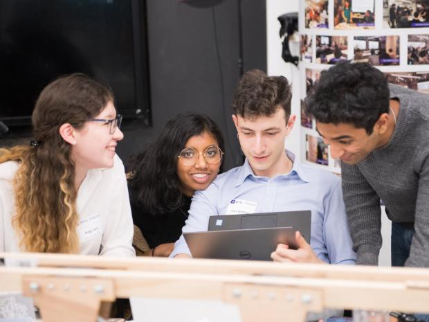 male and female students huddled around laptop smiling male and female students huddled around laptop smiling