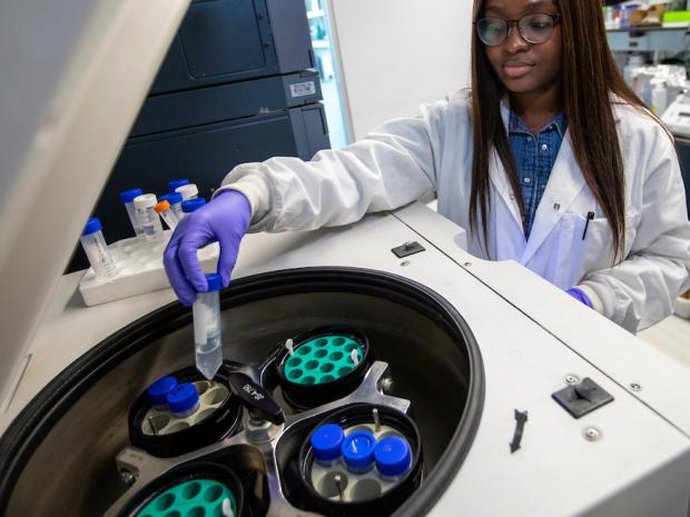 a young Black women in lab gear placing a tube in machine