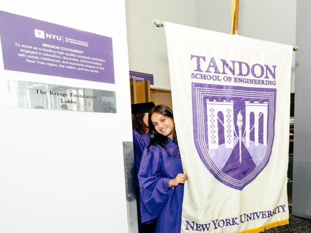 Smiling student peering from behind Tandon banner