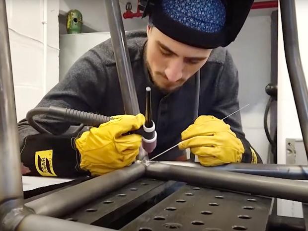 student wearing gloves working on the frame of a motorsport vehicle