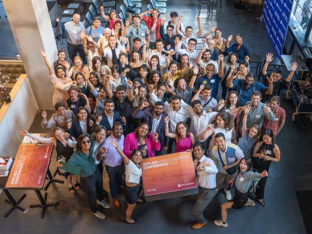 Aerial View of a 50 students with their arms outstretched holding a sign that says Applied Urban Science Conference 2023