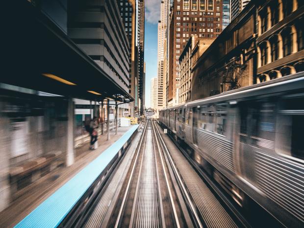 A subway train is moving on an outdoor track in the city. 