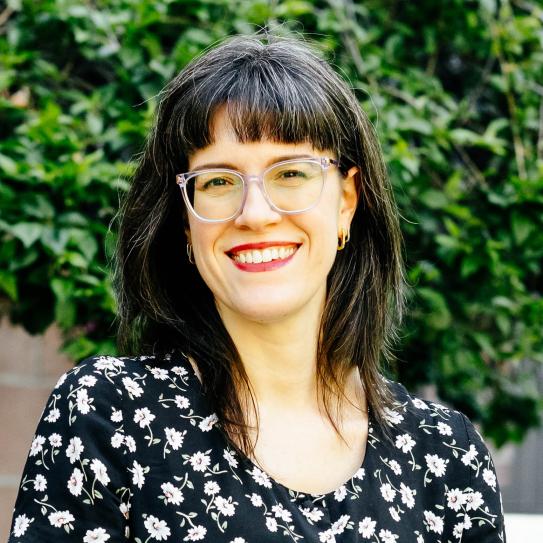 Headshot of a woman smiling in front of greenery.