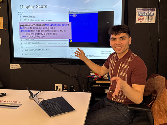 a student sitting with a laptop in front of a large screen with a presentation