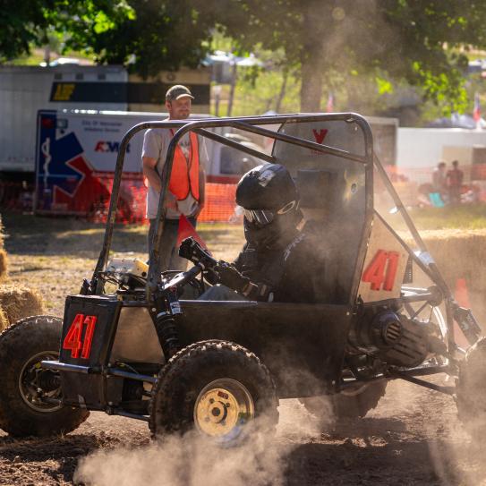 Picture of Baja SAE riding on the dirt road and a few people looking Picture of Baja SAE riding on the dirt road and a few people looking